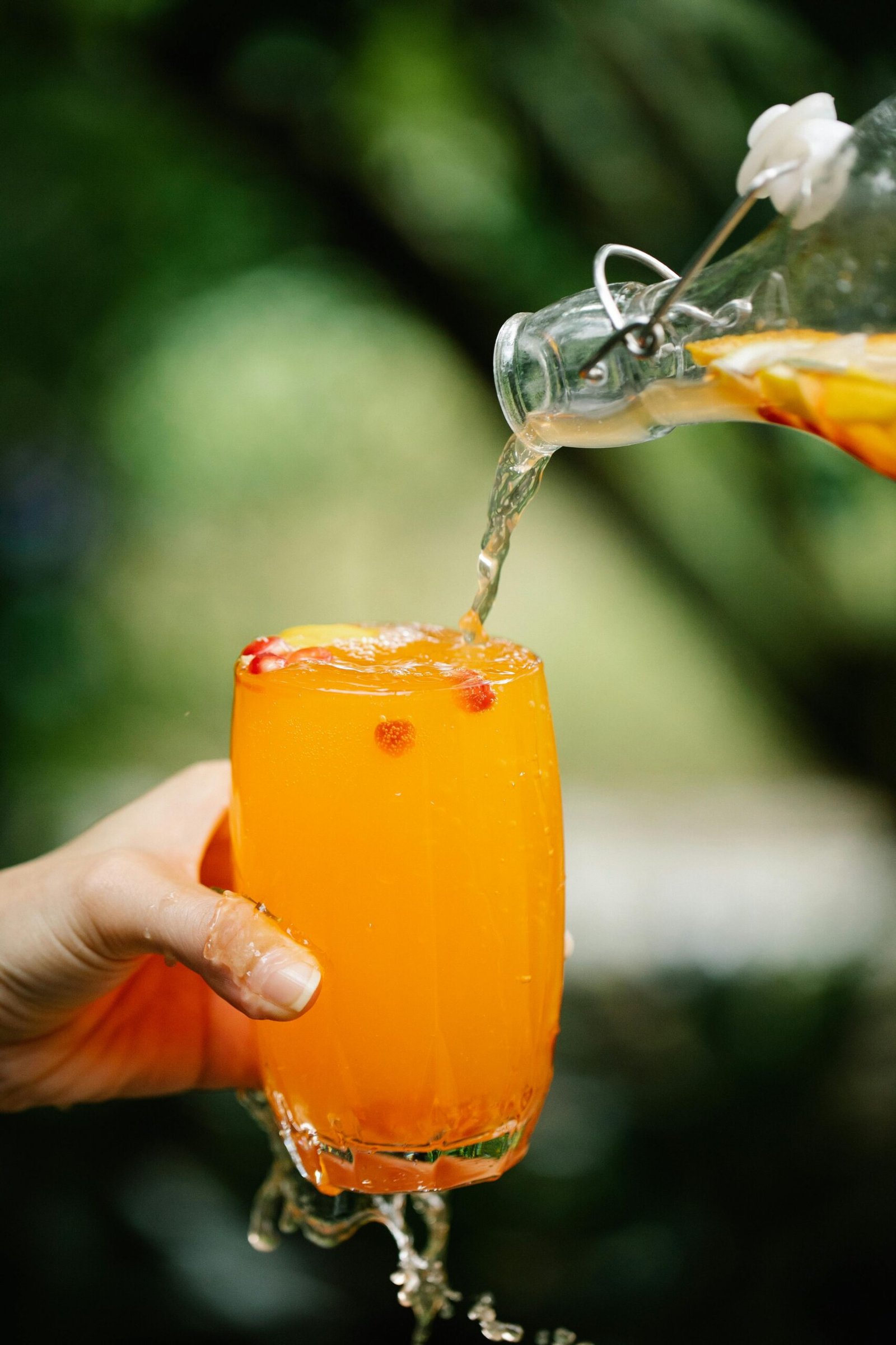 Vibrant orange drink being poured into a glass with lush greenery in the background.