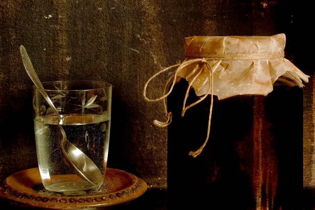 Jar with homemade jam placed with glass of water on shabby table in rural house